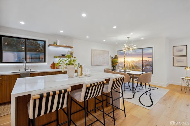 kitchen with a kitchen island, sink, a breakfast bar area, a notable chandelier, and light hardwood / wood-style flooring