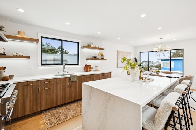 kitchen featuring sink, decorative light fixtures, light wood-type flooring, stainless steel range, and a kitchen island with sink