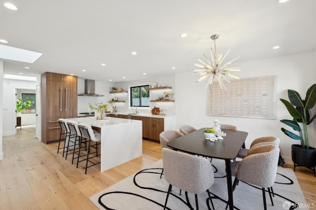 dining area featuring a skylight, sink, light hardwood / wood-style flooring, and a notable chandelier