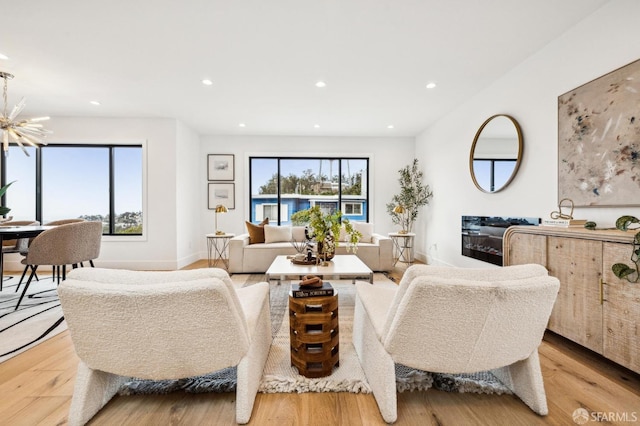 living room with a wealth of natural light, a notable chandelier, and light wood-type flooring