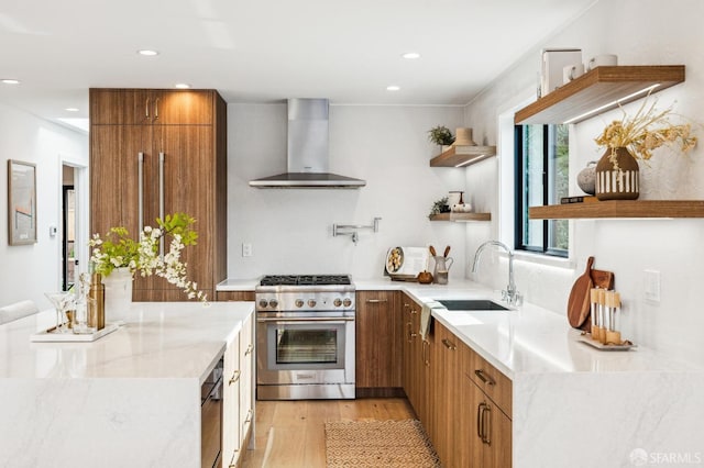 kitchen featuring sink, high end stainless steel range oven, light stone countertops, light wood-type flooring, and wall chimney exhaust hood