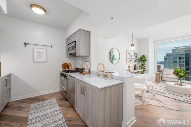 kitchen featuring appliances with stainless steel finishes, kitchen peninsula, sink, light hardwood / wood-style floors, and light stone counters