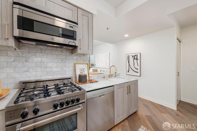 kitchen with sink, light hardwood / wood-style flooring, appliances with stainless steel finishes, light stone countertops, and decorative backsplash