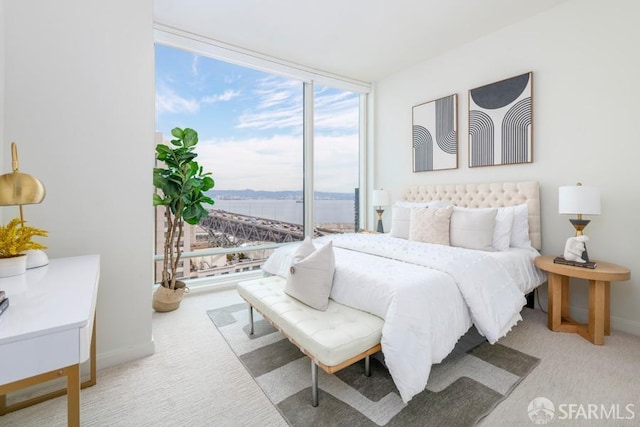 bedroom featuring light colored carpet, expansive windows, and a water view