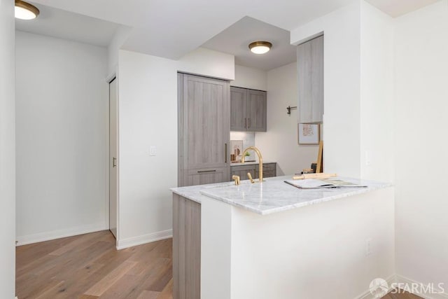 kitchen featuring sink, a kitchen breakfast bar, light stone counters, kitchen peninsula, and light wood-type flooring