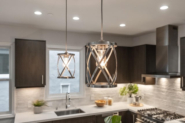 kitchen with wall chimney range hood, sink, dark brown cabinetry, gas stovetop, and decorative light fixtures