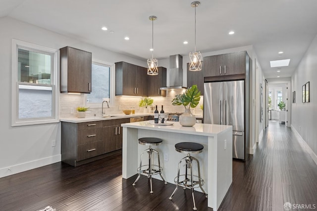 kitchen with wall chimney exhaust hood, a kitchen bar, sink, a center island, and stainless steel refrigerator