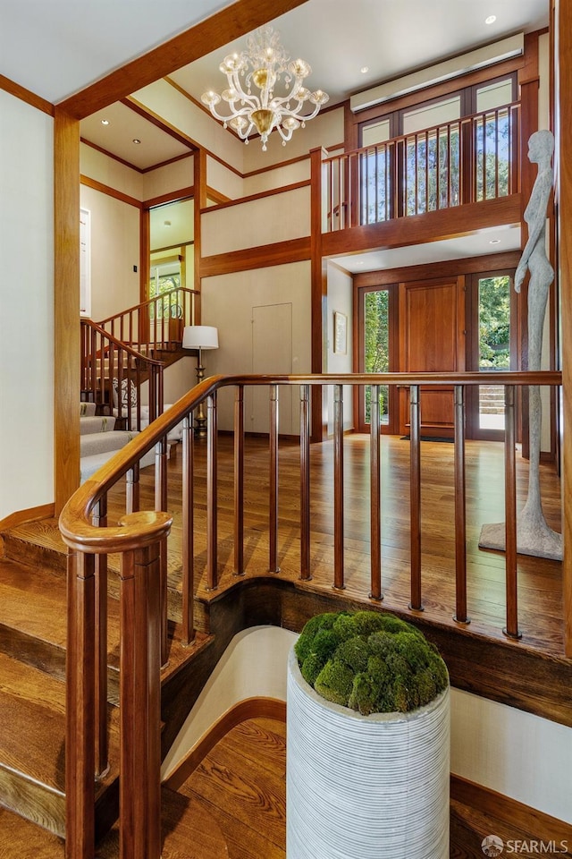 stairs with a chandelier, crown molding, wood finished floors, and baseboards
