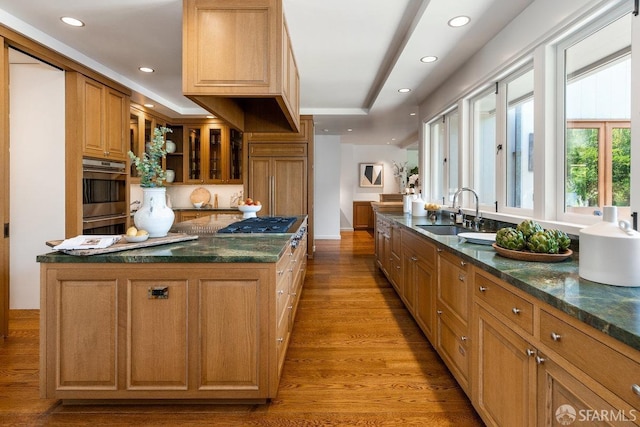 kitchen with dark stone countertops, a sink, light wood finished floors, recessed lighting, and a kitchen island