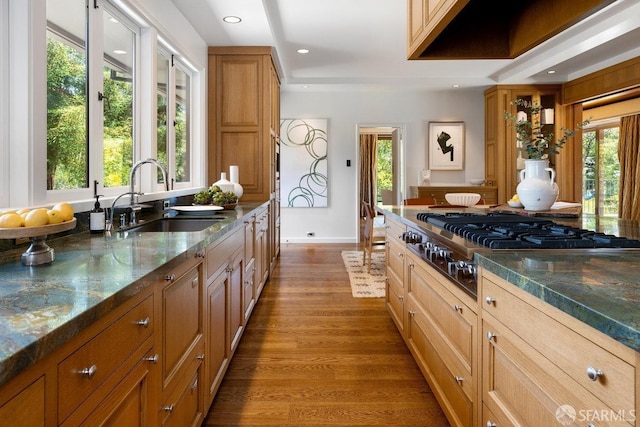 kitchen with dark stone countertops, dark wood-type flooring, stainless steel gas cooktop, brown cabinetry, and a sink