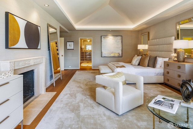 bedroom featuring a tray ceiling, baseboards, wood finished floors, and a high end fireplace