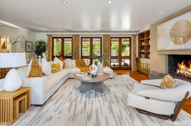 living room featuring built in shelves, recessed lighting, wood finished floors, a lit fireplace, and french doors