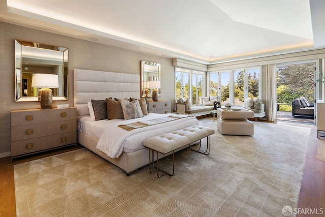 bedroom featuring multiple windows, access to exterior, a raised ceiling, and light wood-style floors