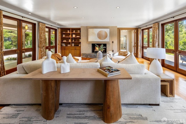 living area featuring a large fireplace, recessed lighting, french doors, built in shelves, and wood finished floors
