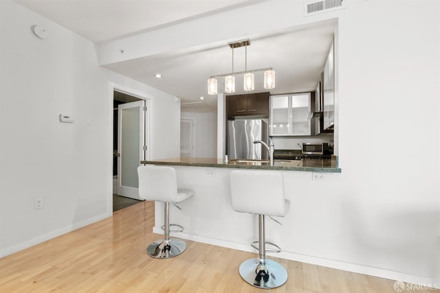 kitchen with a kitchen breakfast bar, light hardwood / wood-style flooring, kitchen peninsula, dark brown cabinetry, and appliances with stainless steel finishes