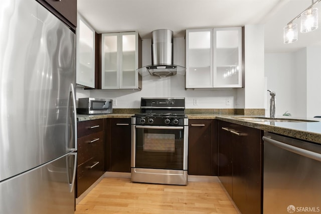 kitchen with wall chimney range hood, appliances with stainless steel finishes, light hardwood / wood-style flooring, and sink