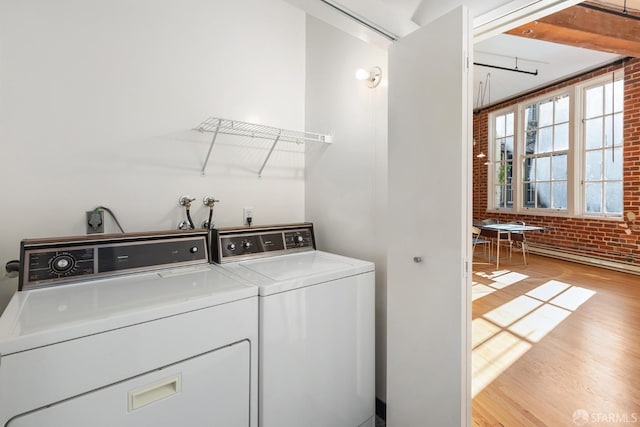 clothes washing area with independent washer and dryer, brick wall, and light hardwood / wood-style flooring