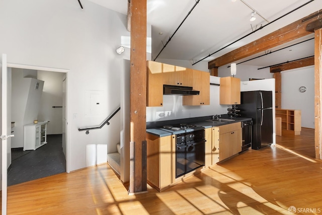 kitchen with black appliances, light wood-type flooring, sink, and a high ceiling