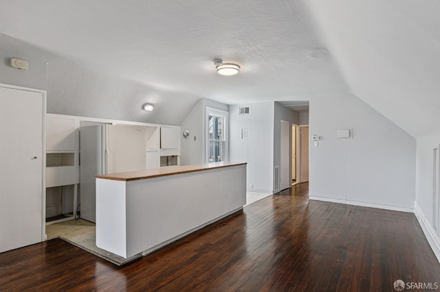 kitchen featuring a textured ceiling, vaulted ceiling, white refrigerator, white cabinets, and hardwood / wood-style floors