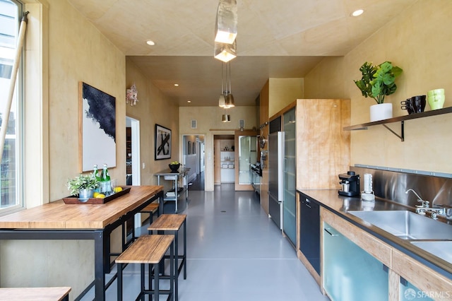 kitchen with sink, hanging light fixtures, wooden counters, high quality fridge, and a breakfast bar