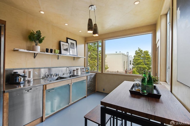 kitchen featuring stainless steel dishwasher, stainless steel counters, sink, concrete floors, and hanging light fixtures