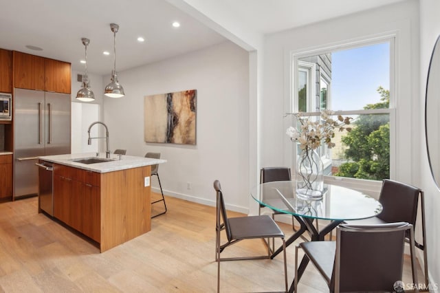 kitchen featuring pendant lighting, sink, built in appliances, light hardwood / wood-style floors, and a center island with sink