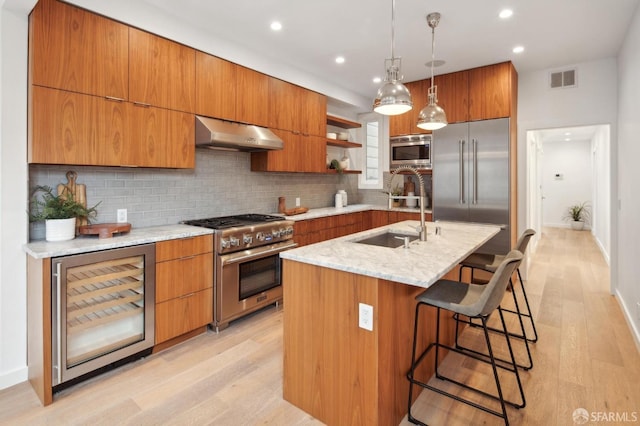 kitchen featuring wine cooler, sink, built in appliances, decorative light fixtures, and an island with sink