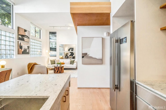 kitchen with track lighting, light hardwood / wood-style flooring, light stone counters, and high end refrigerator