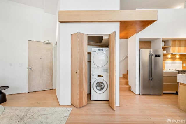 laundry room with light hardwood / wood-style flooring and stacked washer and clothes dryer