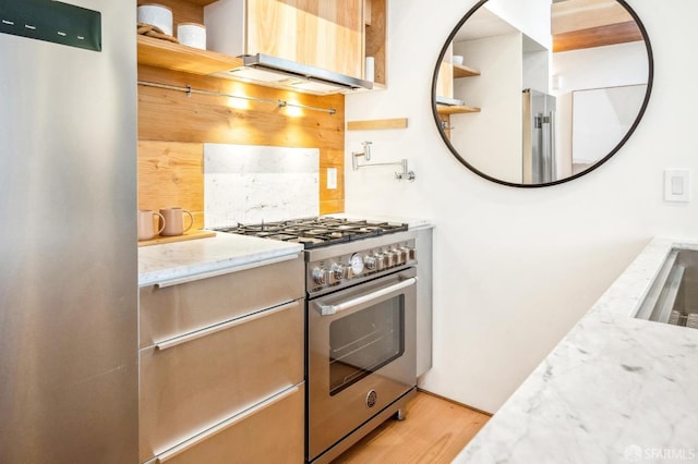 kitchen featuring stainless steel appliances, light stone countertops, light wood-type flooring, and decorative backsplash