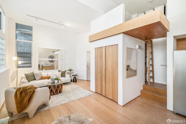 living room with a towering ceiling, track lighting, and light wood-type flooring