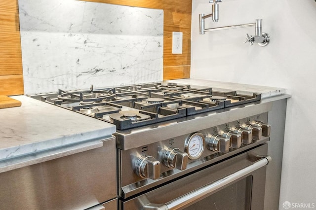 interior details with high end stove, light stone countertops, and backsplash