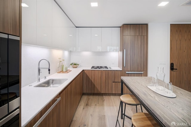 kitchen with sink, white cabinetry, a breakfast bar area, light hardwood / wood-style floors, and decorative backsplash