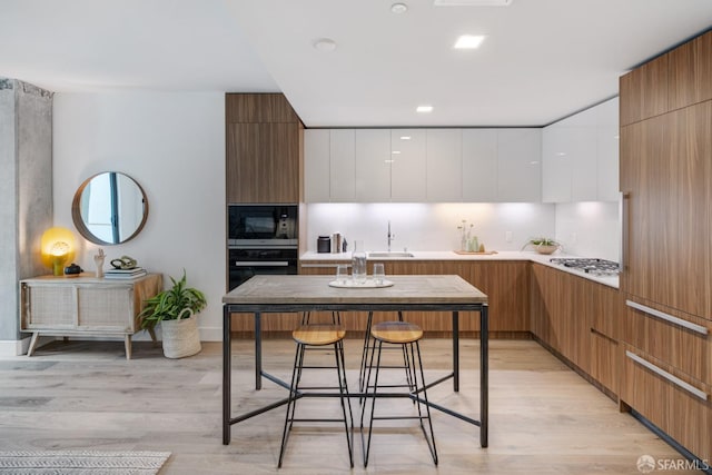 kitchen with white cabinets, black oven, stainless steel microwave, and light hardwood / wood-style floors