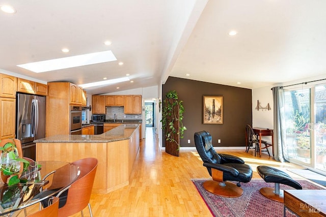 kitchen featuring light wood finished floors, a center island, lofted ceiling with skylight, appliances with stainless steel finishes, and a sink