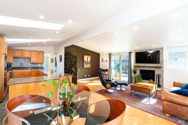 living area featuring a wealth of natural light, vaulted ceiling with skylight, light wood finished floors, and a brick fireplace