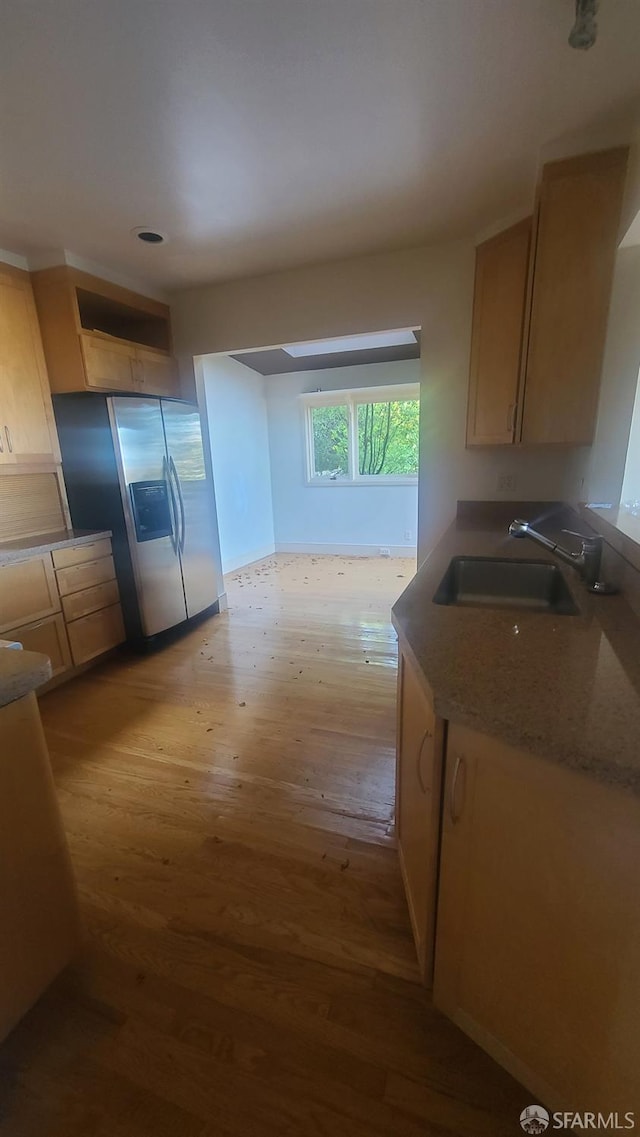 kitchen featuring stainless steel fridge with ice dispenser, light brown cabinetry, dark stone counters, light wood-type flooring, and sink