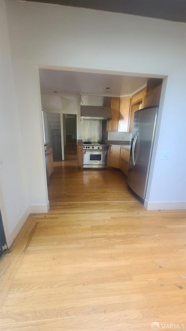 kitchen featuring appliances with stainless steel finishes, wall chimney range hood, and light wood-type flooring