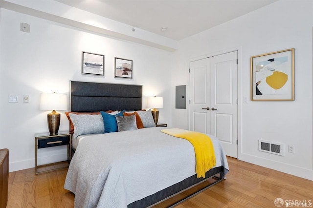 bedroom featuring light wood-style floors, electric panel, visible vents, and baseboards