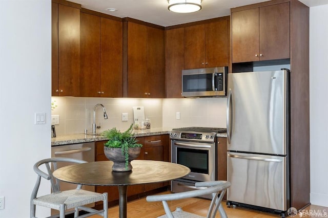 kitchen with light wood finished floors, appliances with stainless steel finishes, light stone counters, backsplash, and a sink