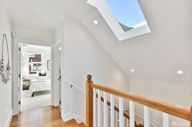 hallway with light hardwood / wood-style floors, lofted ceiling with skylight, and ornamental molding