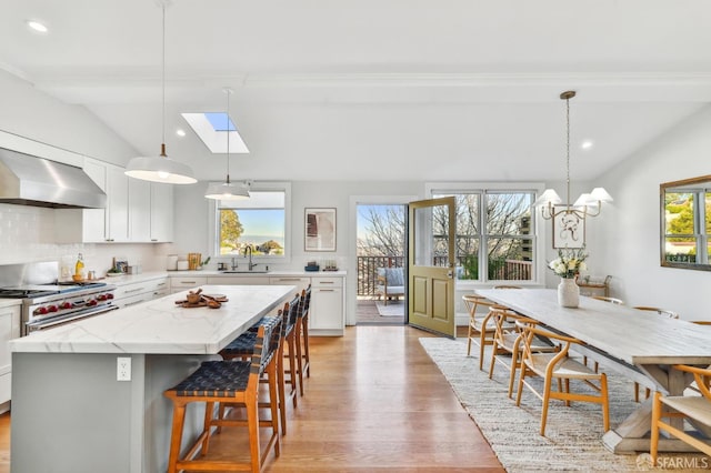 kitchen featuring vaulted ceiling with skylight, a center island, decorative light fixtures, white cabinetry, and decorative backsplash