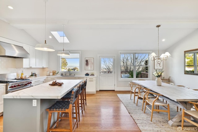 kitchen featuring decorative light fixtures, tasteful backsplash, white cabinetry, vaulted ceiling with skylight, and a kitchen island