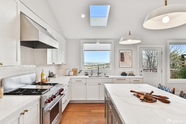 kitchen with decorative light fixtures, sink, white cabinets, light stone counters, and high end stainless steel range oven