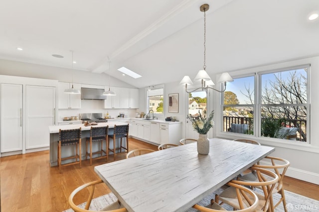 dining space featuring sink, light hardwood / wood-style flooring, and vaulted ceiling with beams