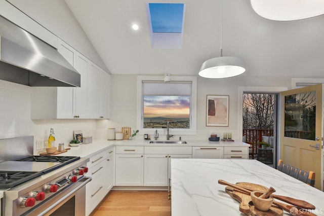 kitchen featuring sink, decorative light fixtures, white cabinetry, exhaust hood, and high end range