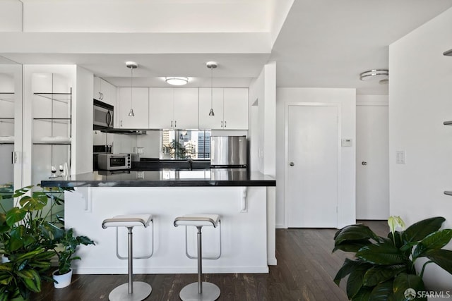 kitchen with appliances with stainless steel finishes, hanging light fixtures, a breakfast bar, white cabinets, and kitchen peninsula