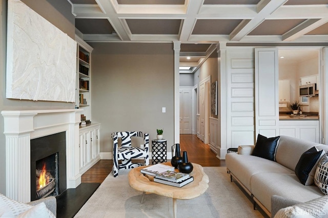 living room featuring coffered ceiling, a lit fireplace, beam ceiling, and dark wood finished floors