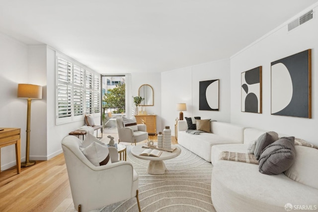 living area featuring light wood finished floors, baseboards, visible vents, and ornamental molding