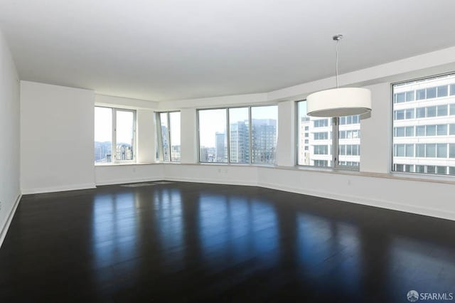 empty room with dark wood finished floors, a city view, and baseboards